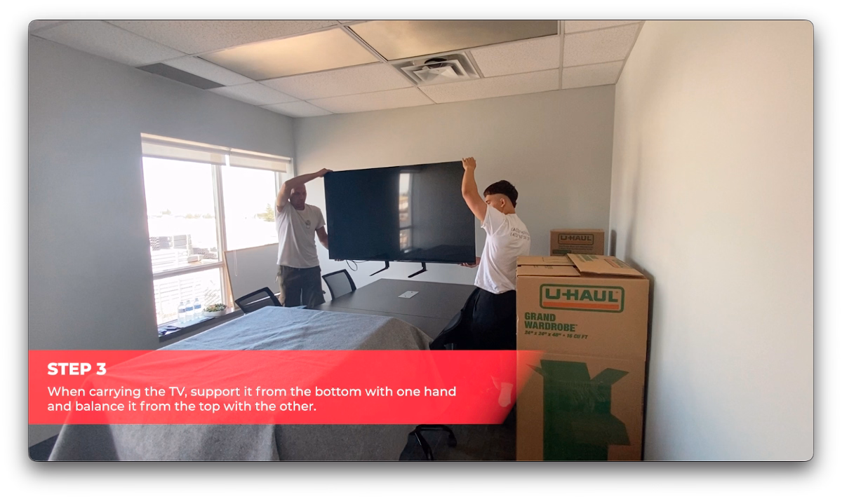 Cactus Moving workers carrying a large flat-screen TV for packing.