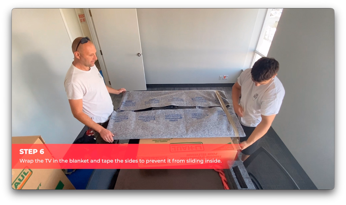 Cactus Moving workers wrapping a flat-screen TV in a moving blanket and securing it with tape.
