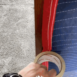Mover shows how to tape a moving blanket on a wooden dresser